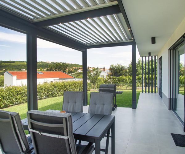 Bioklimatska pergola Misteral na terasi z modernim dizajnom, ki zagotavlja zaščito pred soncem in dežjem.